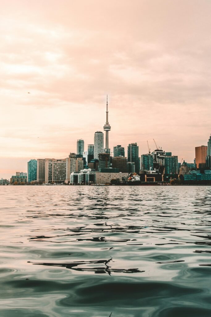 Captivating view of Toronto skyline with CN Tower reflecting on Lake Ontario at sunset.